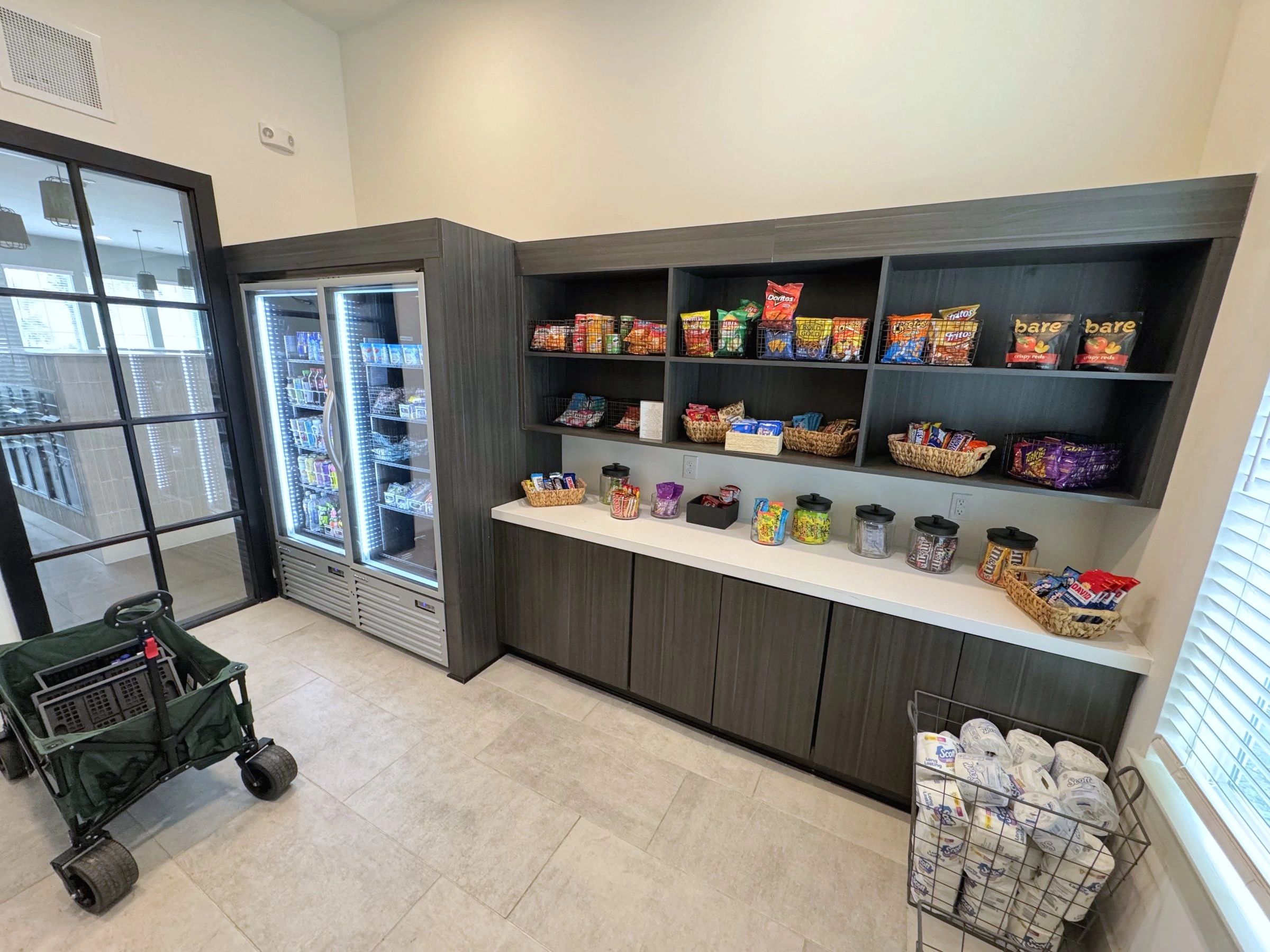 Open-shelf micro market with snacks and drink coolers in a resident amenity room