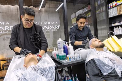 Dos peluqueros cortan el cabello de dos clientes en una barbería.