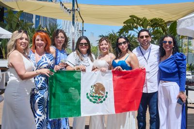 A group of eight people holding a Mexican flag outdoors on a sunny day.