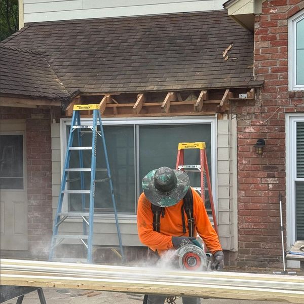 Worker cutting wood with a saw in front of a house under renovation.