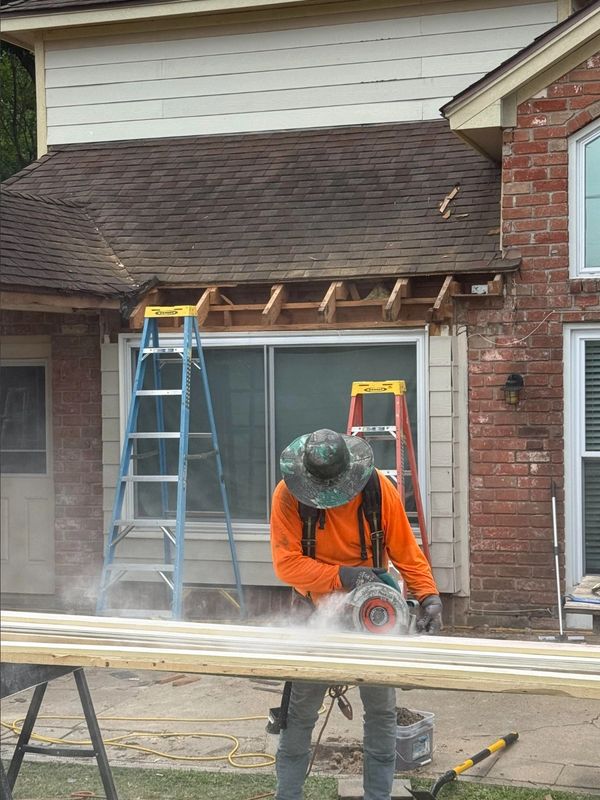 Worker cutting wood with a saw in front of a house under renovation.