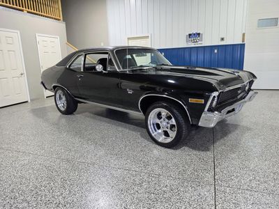 Classic black Chevrolet Nova SS parked indoors with polished chrome wheels.