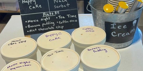 Ice cream tubs labeled with unique flavors next to a metal bucket with spoons.