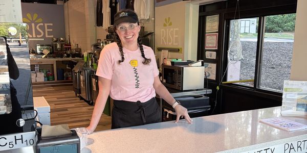 Smiling barista stands behind the counter at Rise café.