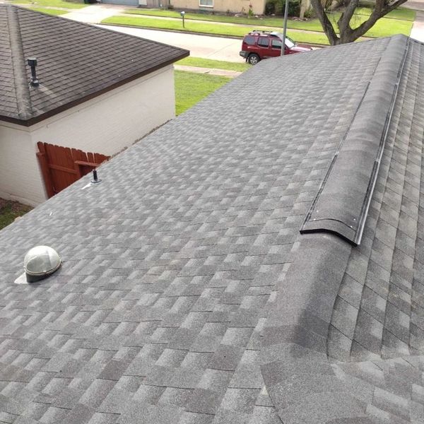 A newly shingled gray rooftop with vents and a nearby house roof.
