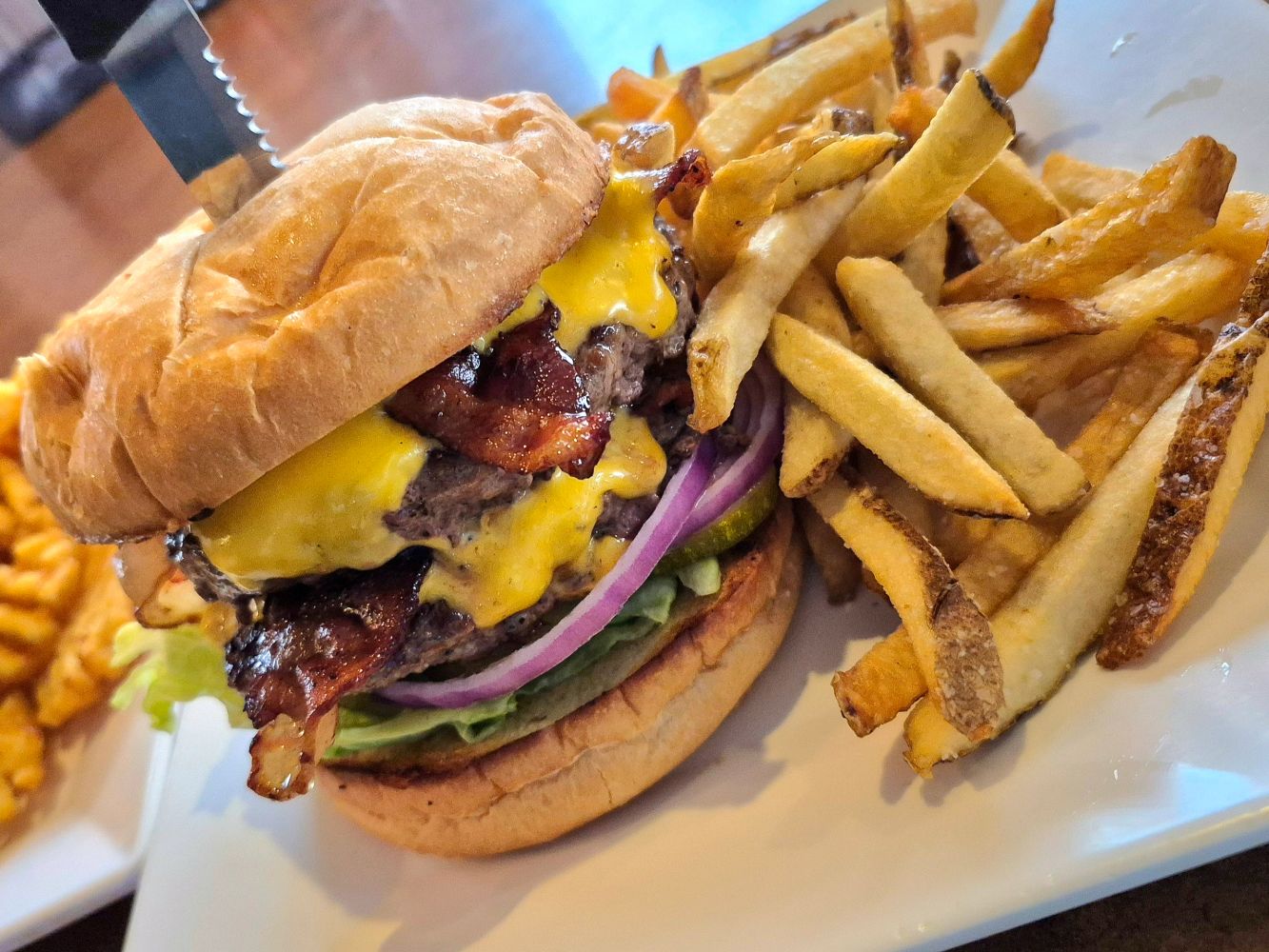 Cheeseburger with bacon and fries on a white plate.