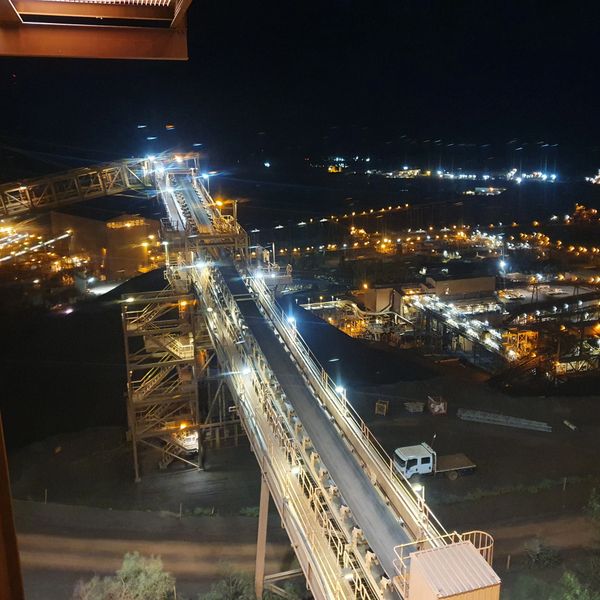 Illuminated industrial conveyor system at night with surrounding factory lights.