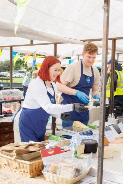 Two vendors selling cheese as a market stall, wearing blue aprons