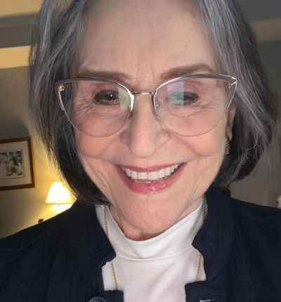 Smiling older woman with glasses taking a selfie indoors.
