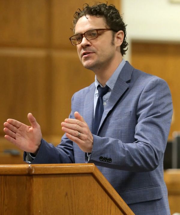 Man wearing glasses and a blue suit speaking indoors.