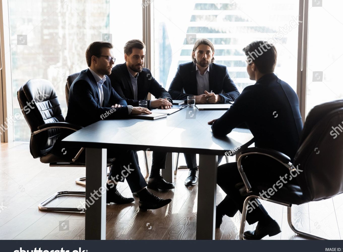 Business interview with four men in suits at a conference table.