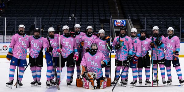 Ice hockey team posing in matching pink and blue uniforms on rink.