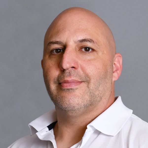 Portrait of a bald man in a white polo shirt against a gray background.