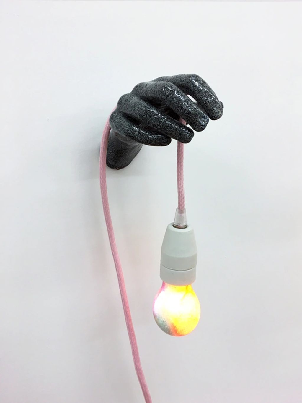 Black hand sculpture holding a pink cord with a lit bulb.