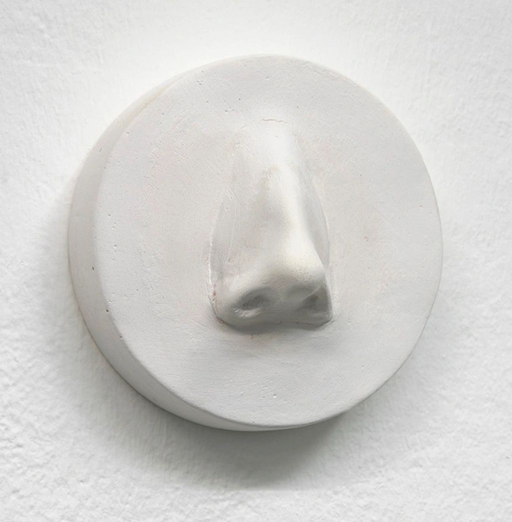 White sculpture of a nose on a circular plaque.