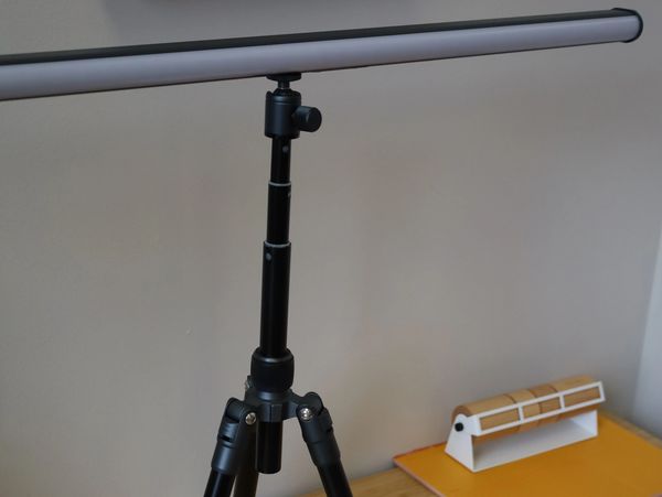 A black tripod lamp on a wooden desk with office supplies.