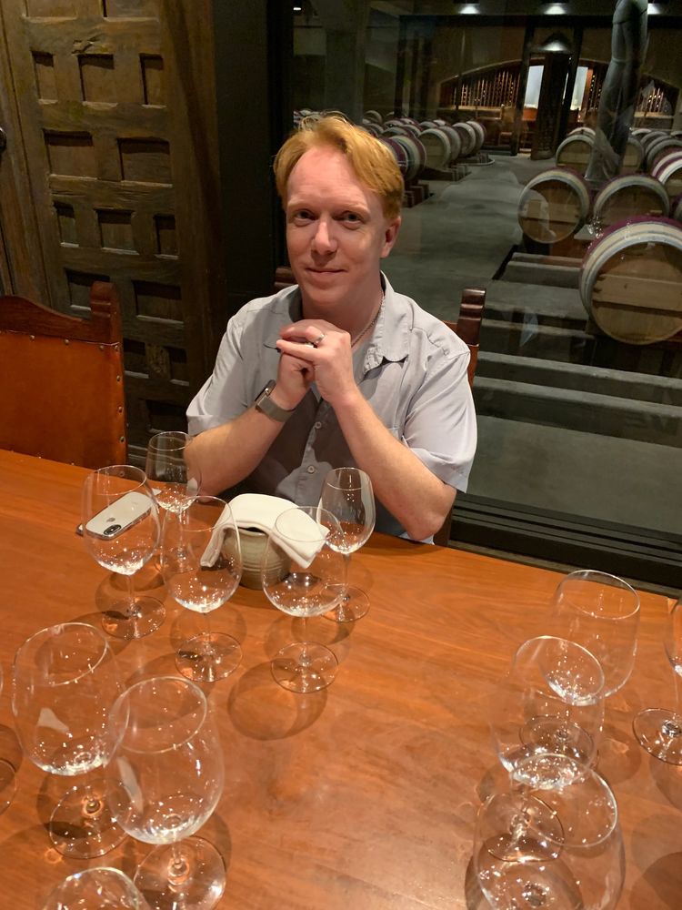 Man sitting at a table with empty wine glasses in a wine cellar.