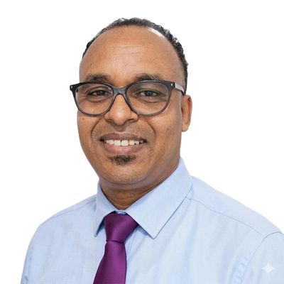 Smiling man wearing glasses, light blue shirt, and purple tie against a white background.