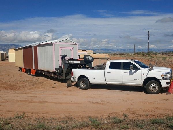 Truck picking up portable sheds on dirt lot – American Barn Co shed transport service