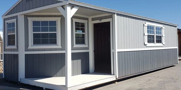 Gray portable shed with covered porch, and multiple windows – cabin-style shed by American Barn Co