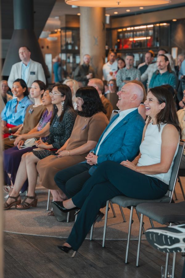 Audience in a conference room enjoying a presentation, smiling and laughing.