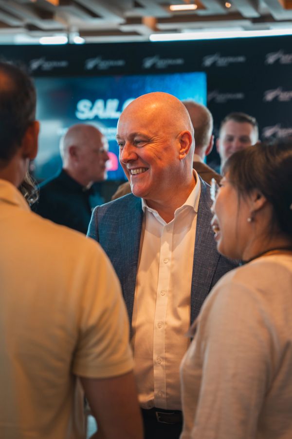A smiling bald man in a suit jacket converses at a social event.