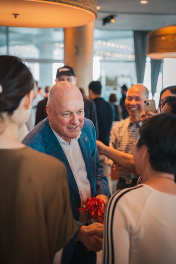 Man in blue blazer warmly shaking hands with people at a social gathering.