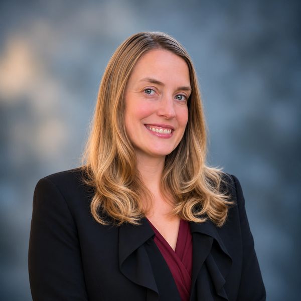 Professional woman smiling in a black blazer with blonde hair.