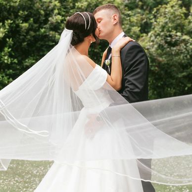 Bride and groom sharing a kiss with flowing veil outdoors.