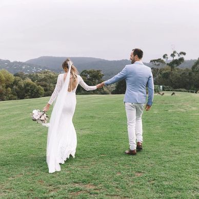 Bride and groom holding hands and walking on grassy hill.