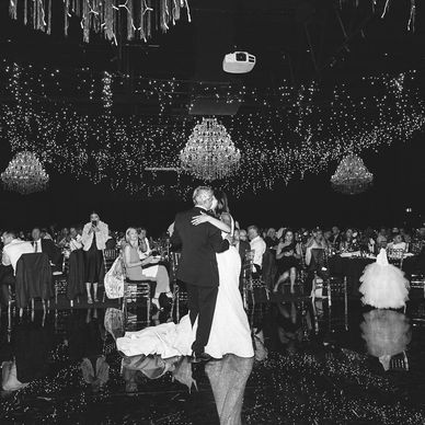 Bride and groom share a dance under twinkling lights and chandeliers.