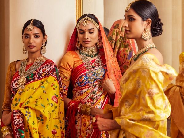 Three women dressed in traditional Indian sarees with intricate jewelry.