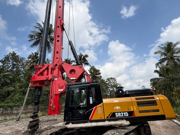 Large drilling machine at a construction site with palm trees and blue sky.
