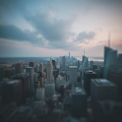 A blurred aerial view of a city skyline at dusk with dramatic clouds.