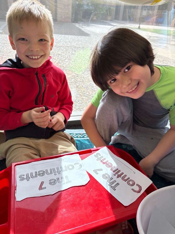 Two boys happily coloring worksheets titled 'The 7 Continents'.