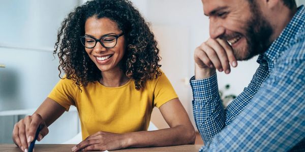Two people smiling and working together at a desk.