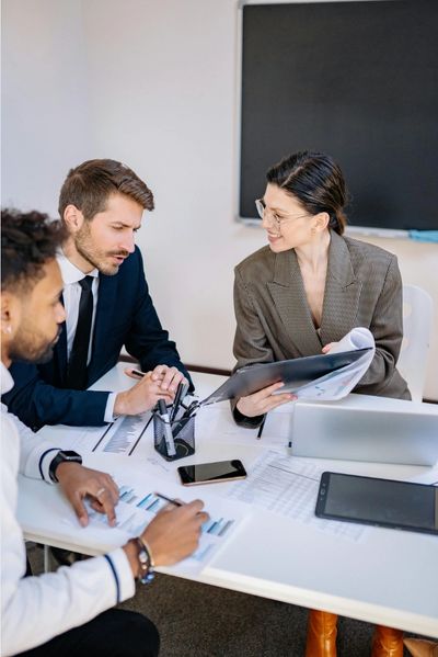 Three professionals collaborating at a table with documents and devices.