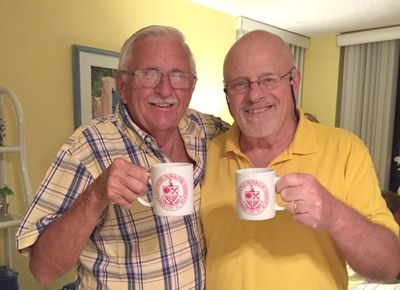 Two smiling men holding mugs and posing indoors.