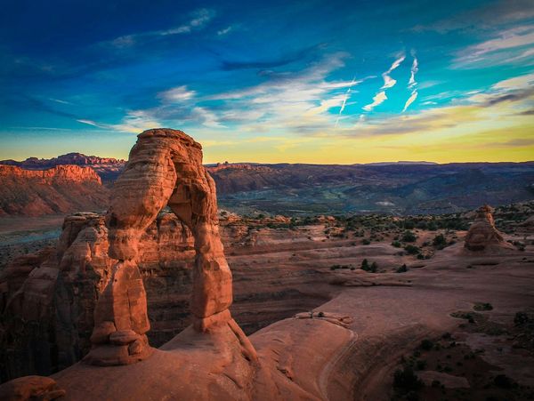 Arches national park arched red rock formation with canyons and blue and yellow sky in the backgroun