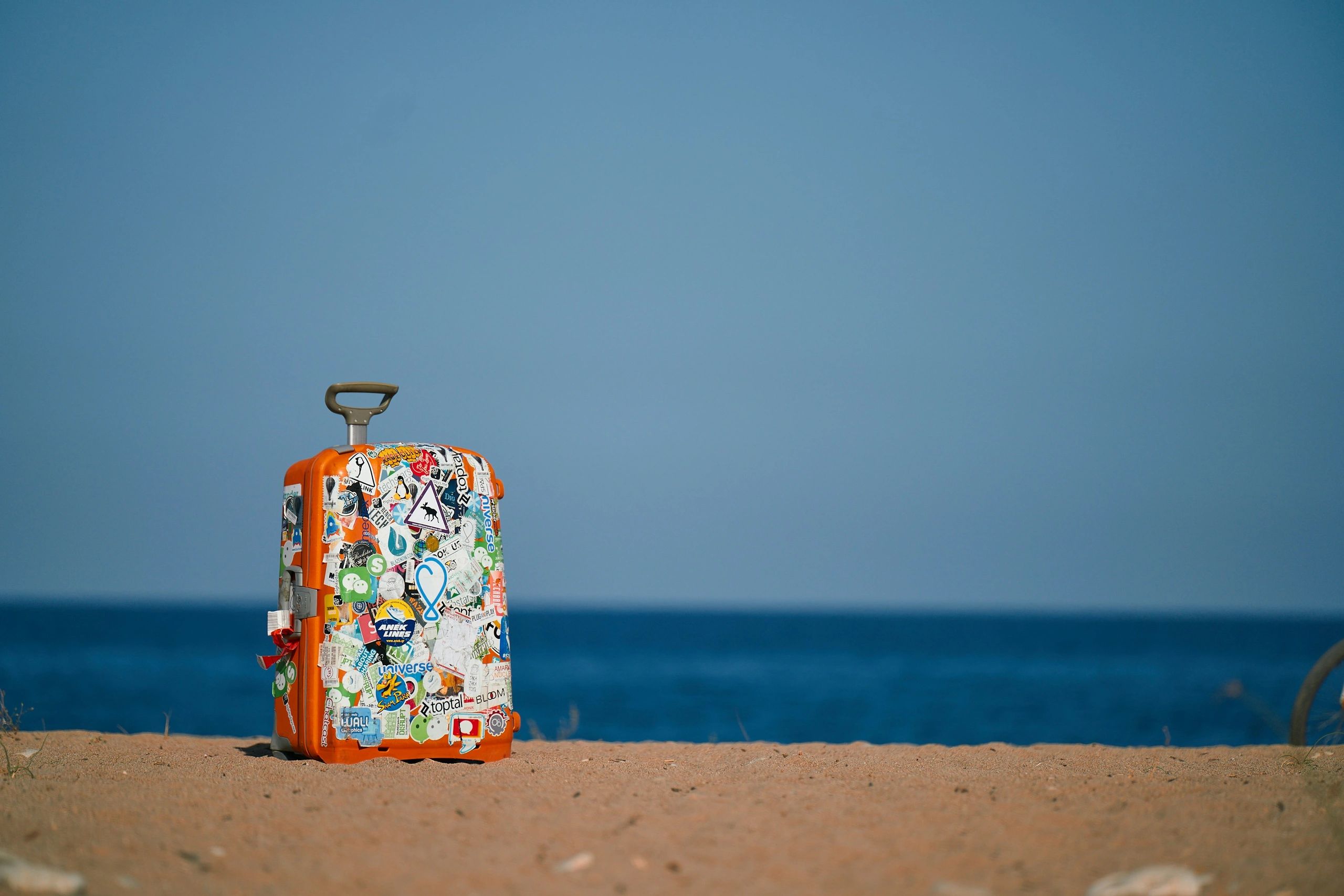 travel suitcase with stickers sitting on a beach by the ocean