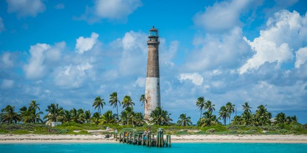 Large lighthouse over aqua ocean and palm trees