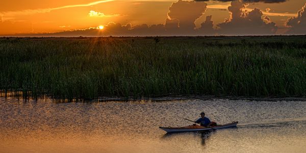 person kayaking in river at sunset