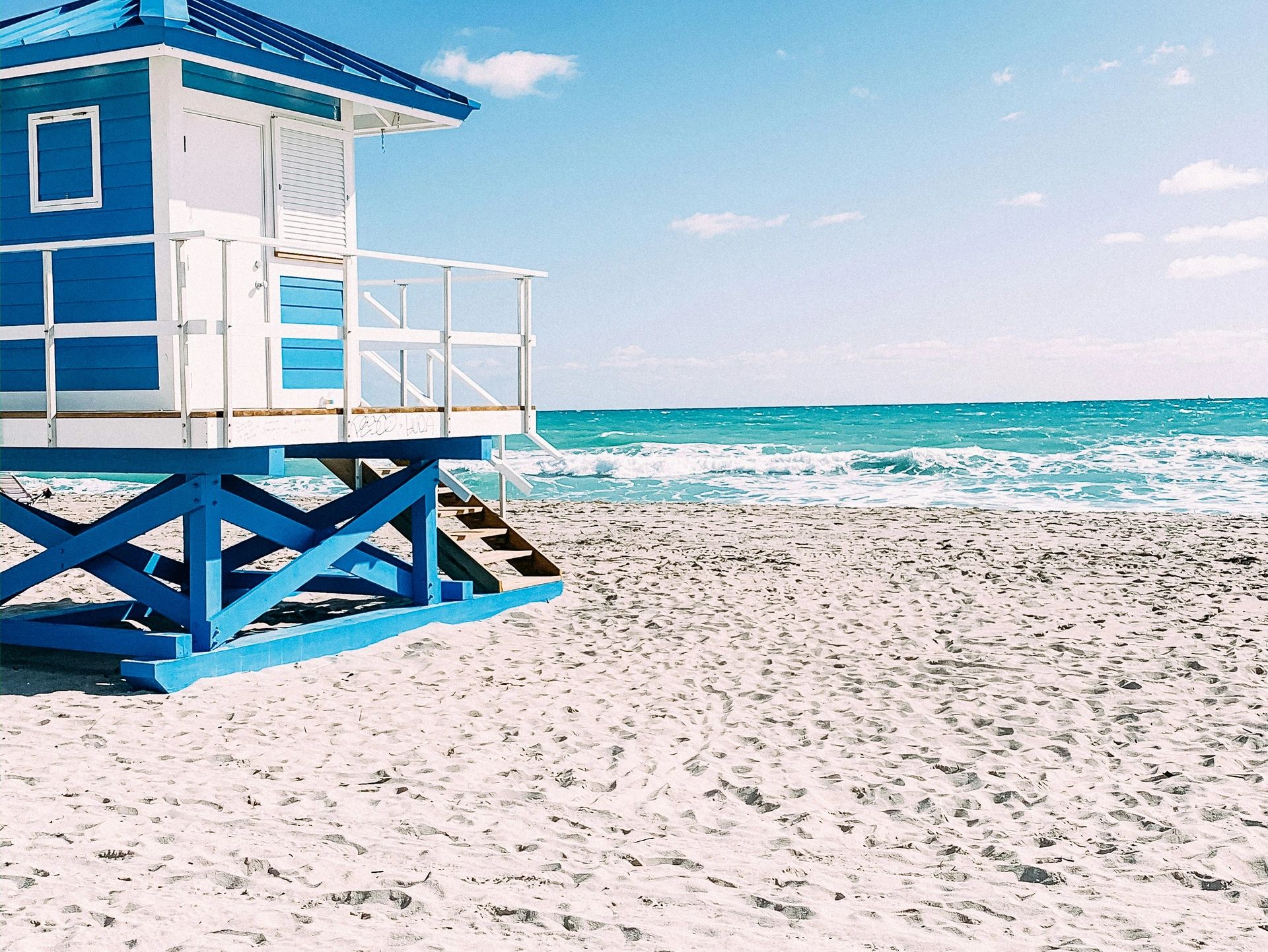 White sand beach with white and blue lifeguard tower in front of blue ocean with waves