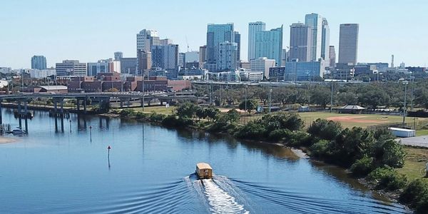 Large river with boat traveling towards large skyscrapers in the distance