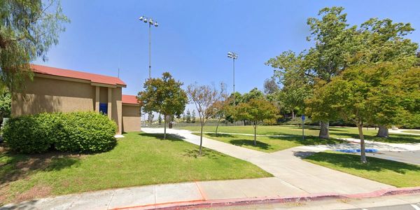 A sunny park area with trees, grass, and a building under a clear blue sky.