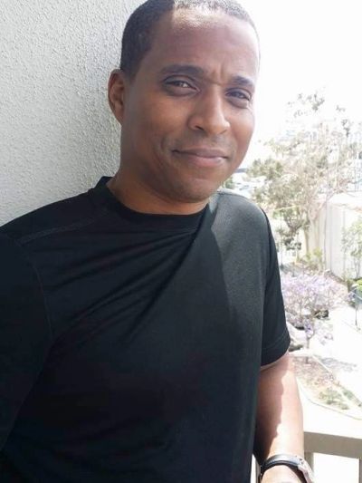 Man in a black shirt standing on a balcony with a slight smile.