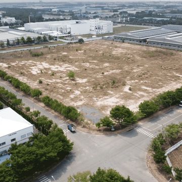 A large vacant plot of land in an industrial area with surrounding buildings.