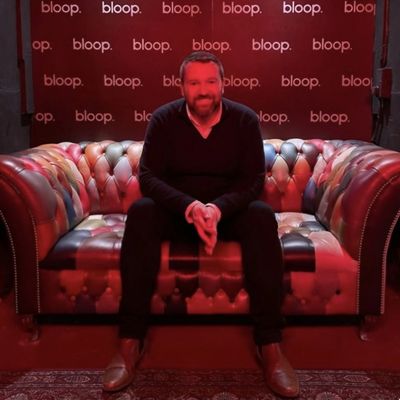 Man sitting on a patterned leather couch under red lighting.