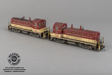 Two detailed model trains painted in maroon and cream colors connected on a gray surface.