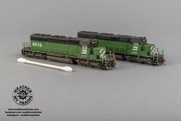Two detailed green model trains placed beside a cotton swab for scale.